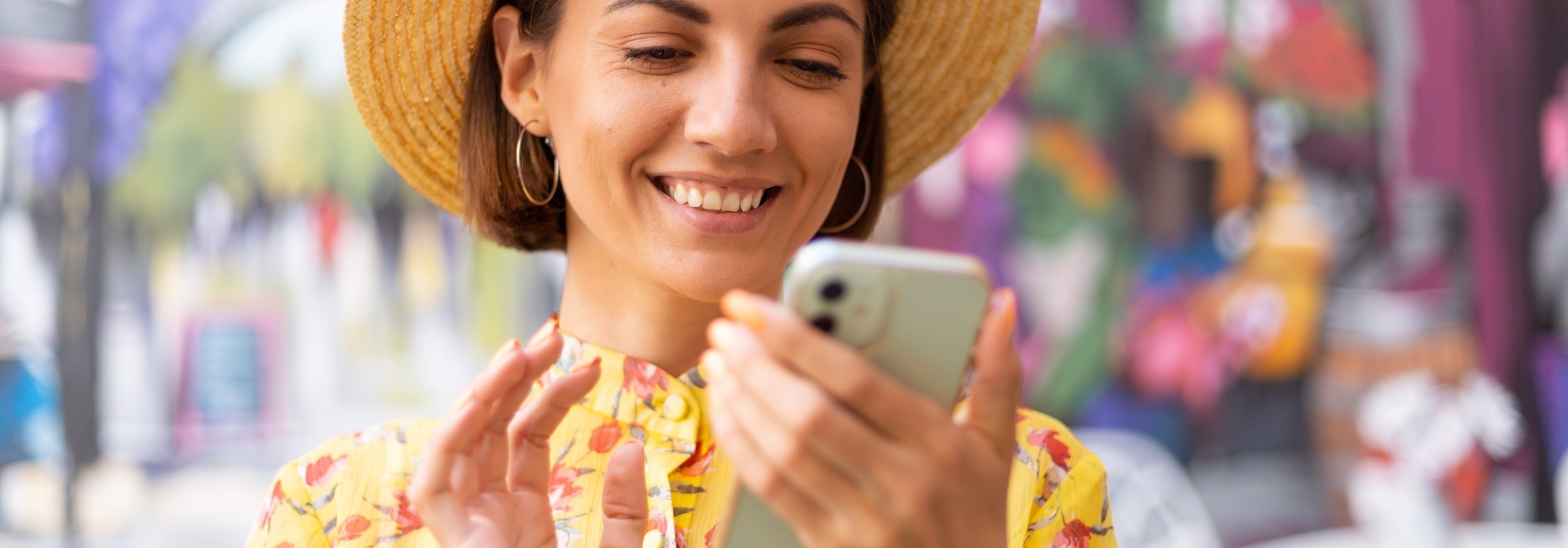 Outdoor fashion portrait of woman in yellow summer dress on background of street wall colorful art picture, typing, searching on mobile phone, positive smile